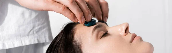 Panoramic shot of healer standing near woman with closed eyes and using stones — Stock Photo