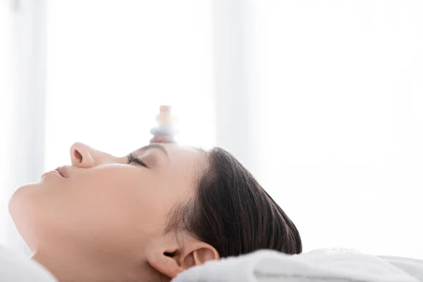 Woman lying with closed eyes with stones on forehead — Stock Photo