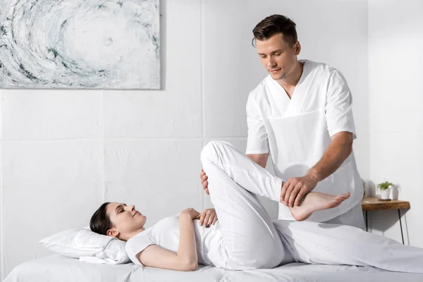 Concentré masseur debout près de la femme et toucher sa jambe — Photo de stock