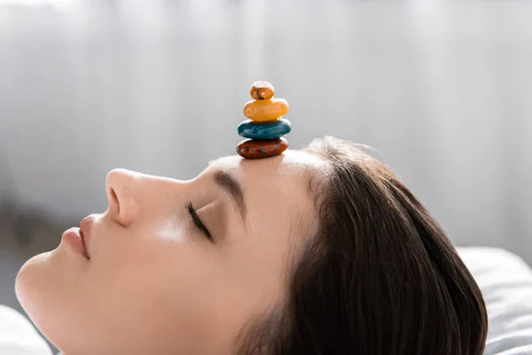 Woman lying with closed eyes with colorful stones on forehead — Stock Photo