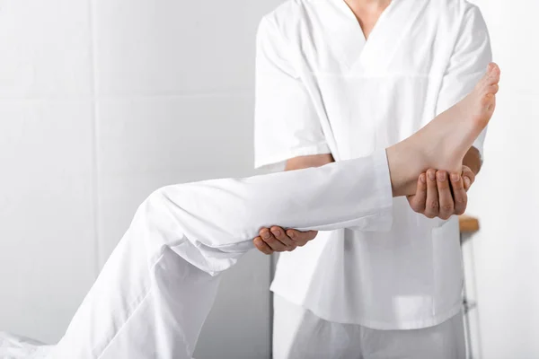 Vista cortada de massagista em pé perto da mulher e tocando sua perna — Fotografia de Stock