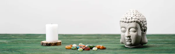 Panoramic shot of buddha statuette, candle and colorful semiprecious stones on wooden surface isolated on white — Stock Photo
