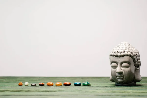 Buddha statuette and colorful semiprecious stones on wooden surface isolated on grey — Stock Photo