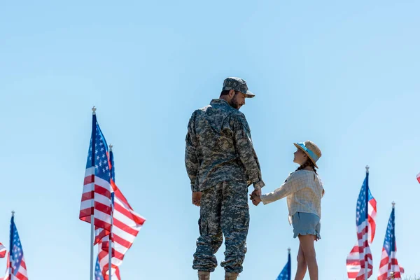 Батько у військовій формі тримає руки з милою дочкою біля американських прапорів — стокове фото
