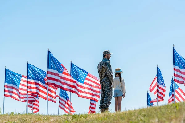 Homem de uniforme militar de pé com a filha perto de bandeiras americanas — Fotografia de Stock