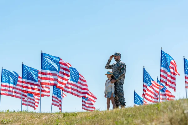 Selective focus of father in military uniform standing with cute kid near american flags — Stock Photo