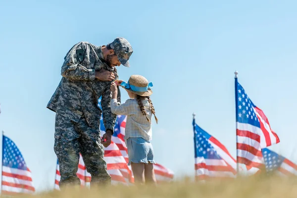 Fuoco selettivo del capretto che tocca l'uniforme del padre militare vicino alle bandiere americane — Foto stock