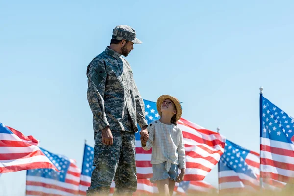 Enfoque selectivo de niño cogido de la mano con el padre militar cerca de banderas americanas - foto de stock