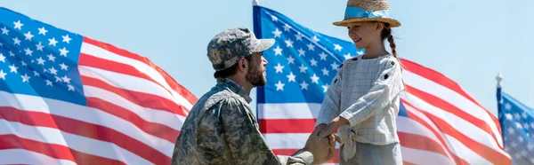 Tiro panorâmico de pai militar de mãos dadas com criança feliz perto de bandeiras americanas — Fotografia de Stock