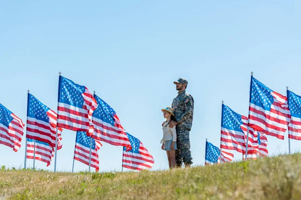 Selektiver Fokus des Vaters in Militäruniform, der mit süßem Kind neben amerikanischen Flaggen steht — Stockfoto