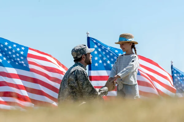 Messa a fuoco selettiva del padre militare che si tiene per mano con bambino felice vicino alle bandiere americane — Foto stock