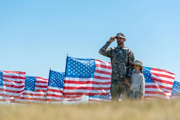 Foco seletivo do homem militar tocando cap perto de crianças e bandeiras americanas — Fotografia de Stock