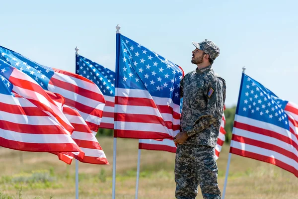 Man in military uniform and cap standing and touching american flag — Stock Photo
