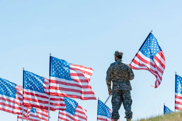 Selective focus of man in military uniform and cap standing and holding american flag — Stock Photo