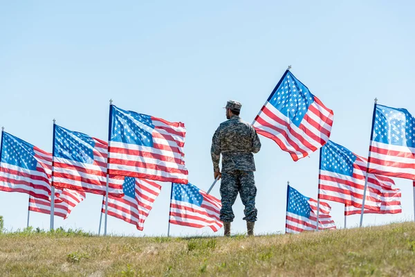 Fuoco selettivo del soldato in uniforme militare e cap in piedi e con bandiera americana — Foto stock