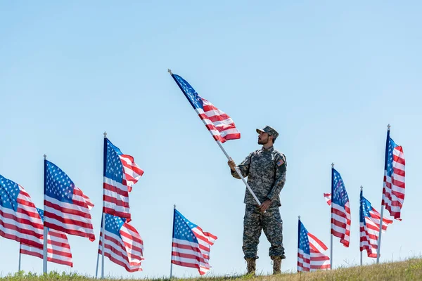 Foyer sélectif du beau soldat en uniforme militaire et casquette tenant drapeau américain — Photo de stock