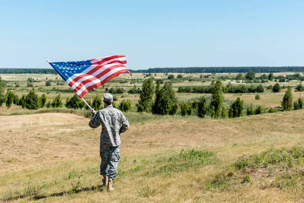 Военный в форме, стоящий на траве и держащий американский флаг — стоковое фото