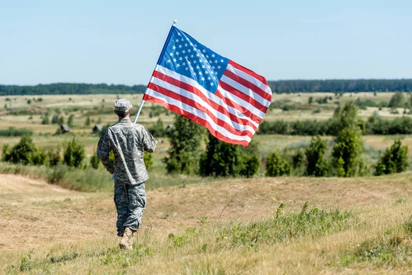 Homem militar de uniforme andando na grama e segurando bandeira americana — Fotografia de Stock