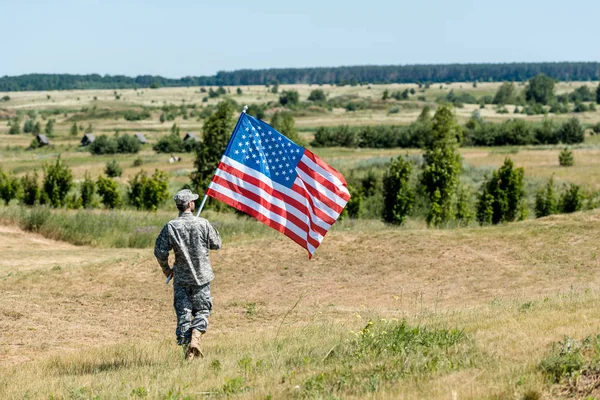 Солдат в форме ходит по траве и держит американский флаг — стоковое фото