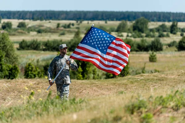 Selective focus of handsome military man in uniform and cap holding american flag — Stock Photo