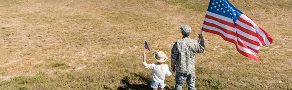 Plano panorámico de militar y patriótico niño sosteniendo banderas americanas - foto de stock