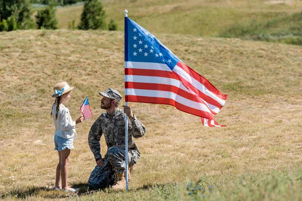 Cute kid holding american flag and looking at handsome military father — Stock Photo