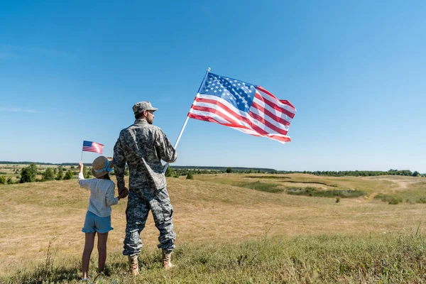 Soldado cogido de la mano con el niño y sosteniendo la bandera americana - foto de stock