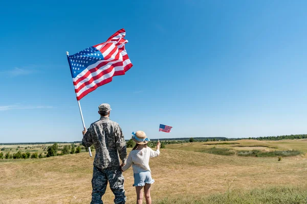 Vue arrière du père militaire et de l'enfant patriotique tenant des drapeaux américains — Photo de stock
