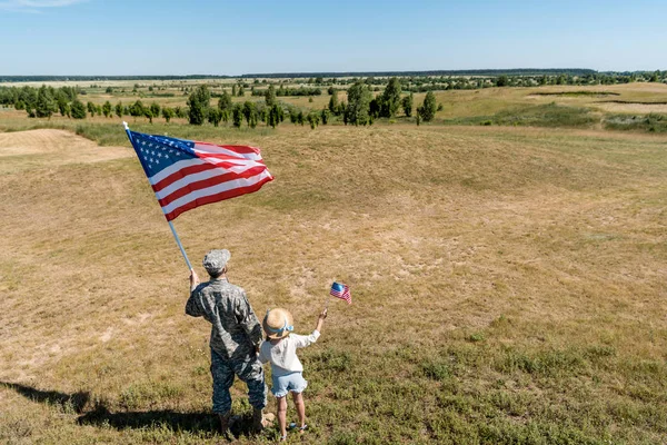 Vue arrière du père militaire et de l'enfant patriotique tenant des drapeaux américains — Photo de stock