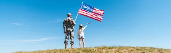 Plano panorámico de niño y padre militar sosteniendo banderas americanas - foto de stock