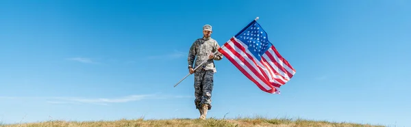 Plano panorámico del guapo militar en uniforme sosteniendo bandera americana con estrellas y rayas - foto de stock