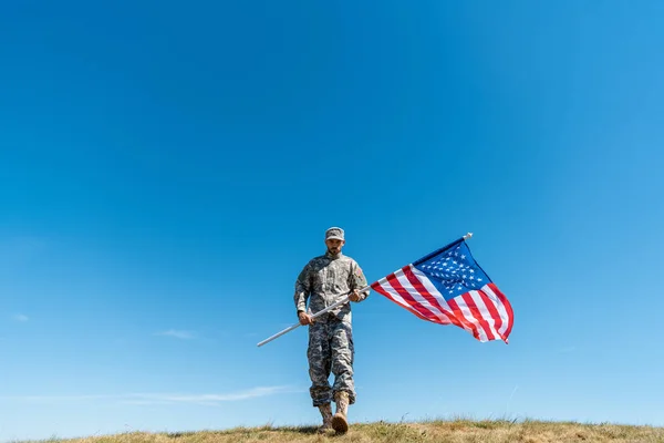 Handsome soldier in uniform walking with american flag — Stock Photo