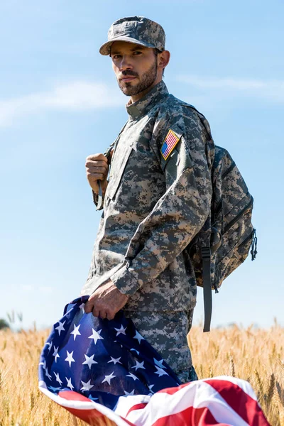 Foco seletivo do soldado em uniforme segurando bandeira americana enquanto está em campo — Fotografia de Stock