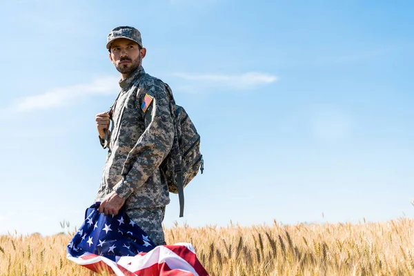 Selective focus of soldier in uniform holding american flag while standing in field — Stock Photo