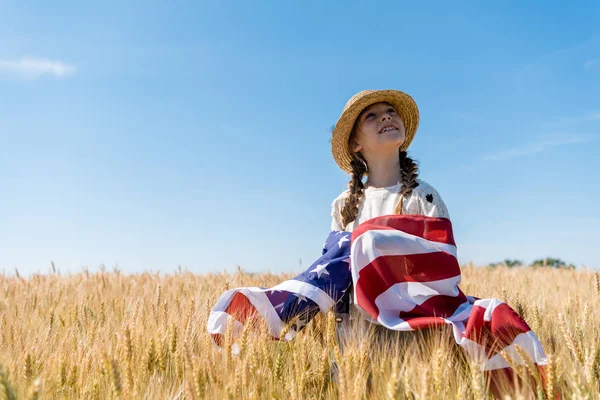 Enfant souriant en chapeau de paille tenant drapeau américain dans un champ doré avec du blé — Photo de stock