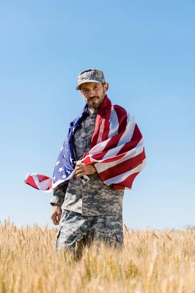 Foco seletivo de soldado bonito em boné e uniforme segurando bandeira americana no campo — Fotografia de Stock