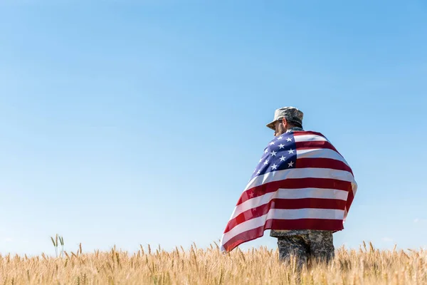 Soldier in cap and military uniform holding american flag in golden field — Stock Photo