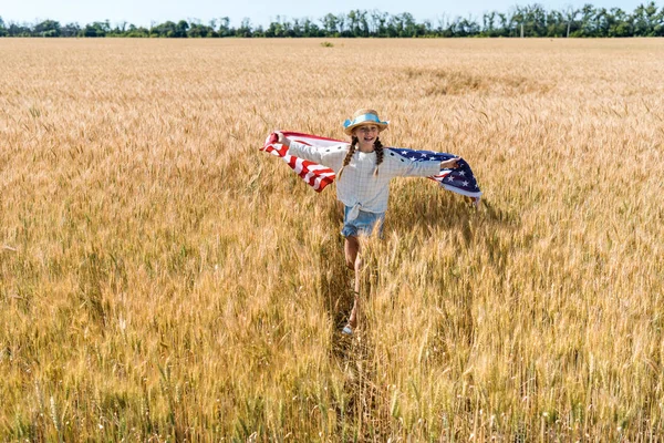 Lindo y feliz niño sosteniendo bandera americana con estrellas y rayas en el campo de oro - foto de stock