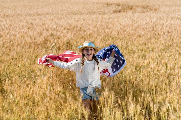 Criança alegre segurando bandeira americana com estrelas e listras no campo dourado — Fotografia de Stock