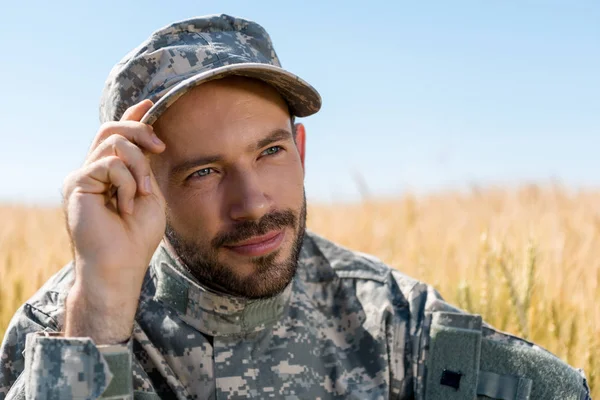 Soldato positivo in uniforme militare toccare cappello e sorridere in campo — Foto stock