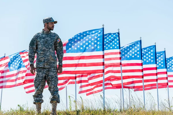 Soldado patriótico en uniforme de pie cerca de banderas americanas y el cielo azul - foto de stock
