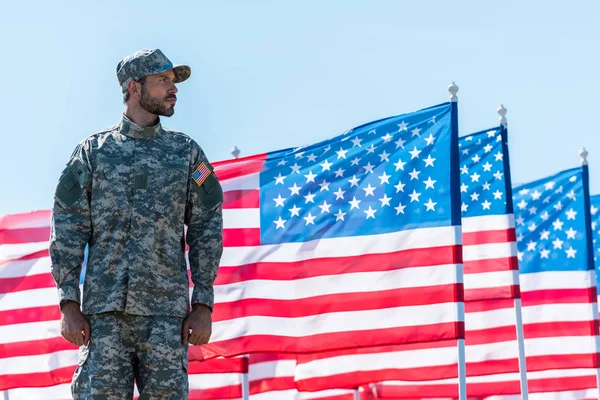 Солдат в форме стоит рядом с американскими флагами на фоне голубого неба — стоковое фото