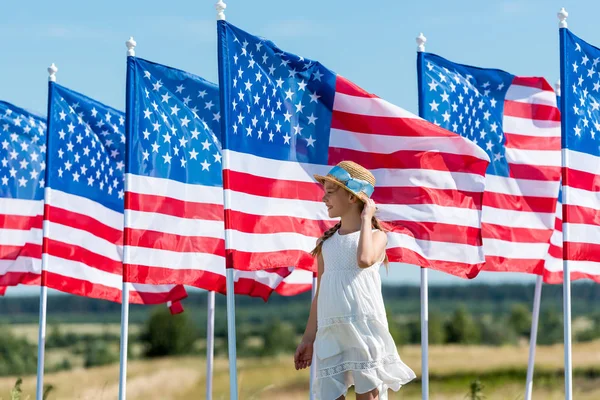 Милый патриотический ребенок, стоящий в белом платье возле американских флагов — стоковое фото