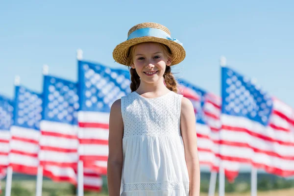 Happy child standing in dress and straw hat near american flags — Stock Photo