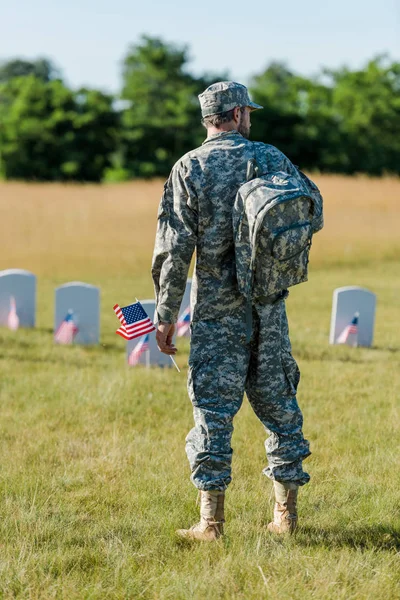Military man holding american flag near headstones in graveyard — Stock Photo