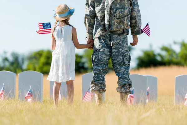 Cropped view of military man and patriotic child holding hands and american flags — Stock Photo