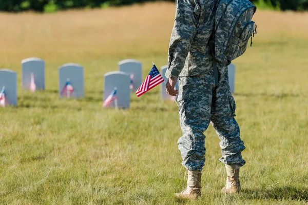 Обрізаний вид солдата, який тримає американський прапор біля надгробків на кладовищі — стокове фото