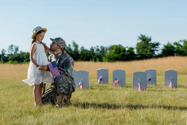 Uomo militare in berretto seduto vicino a bambino in cappello di paglia e lapidi nel cimitero — Foto stock