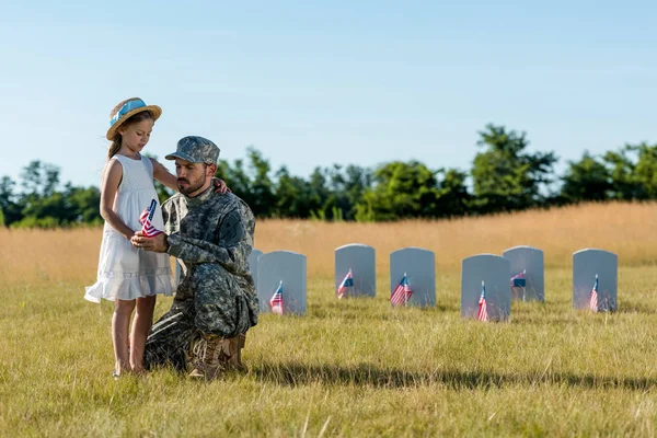 Military man in uniform sitting near child and headstones in graveyard — Stock Photo
