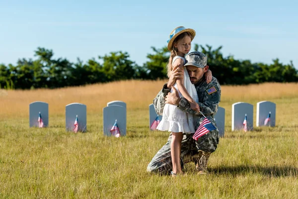 Military man in uniform hugging child near headstones in graveyard — Stock Photo